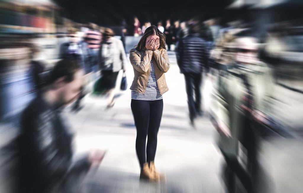 woman covering her face in the middle of a crowd suffering from anxiety and addiction