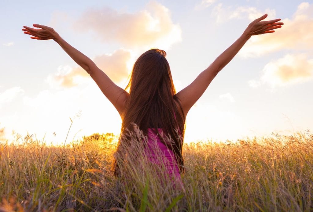 woman walking through a field with her hands up for gratitude in recovery