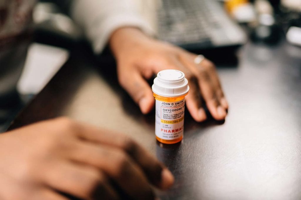 A woman stares at a pill bottle and wonders if there is an opioid crisis in America