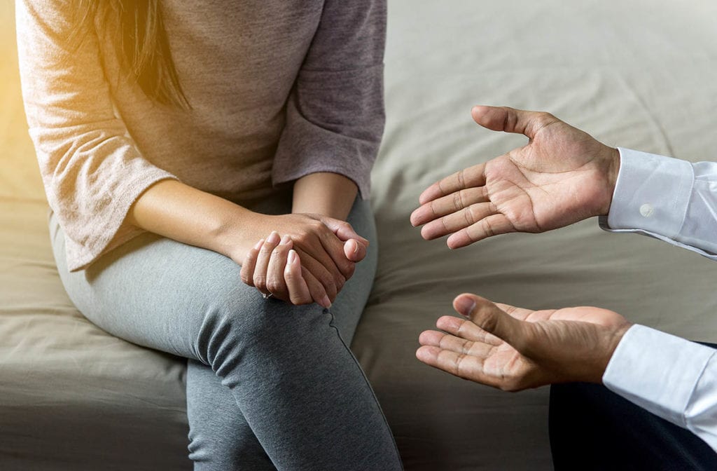 close up of hands gesturing while explaining inpatient vs outpatient rehab to woman sitting down