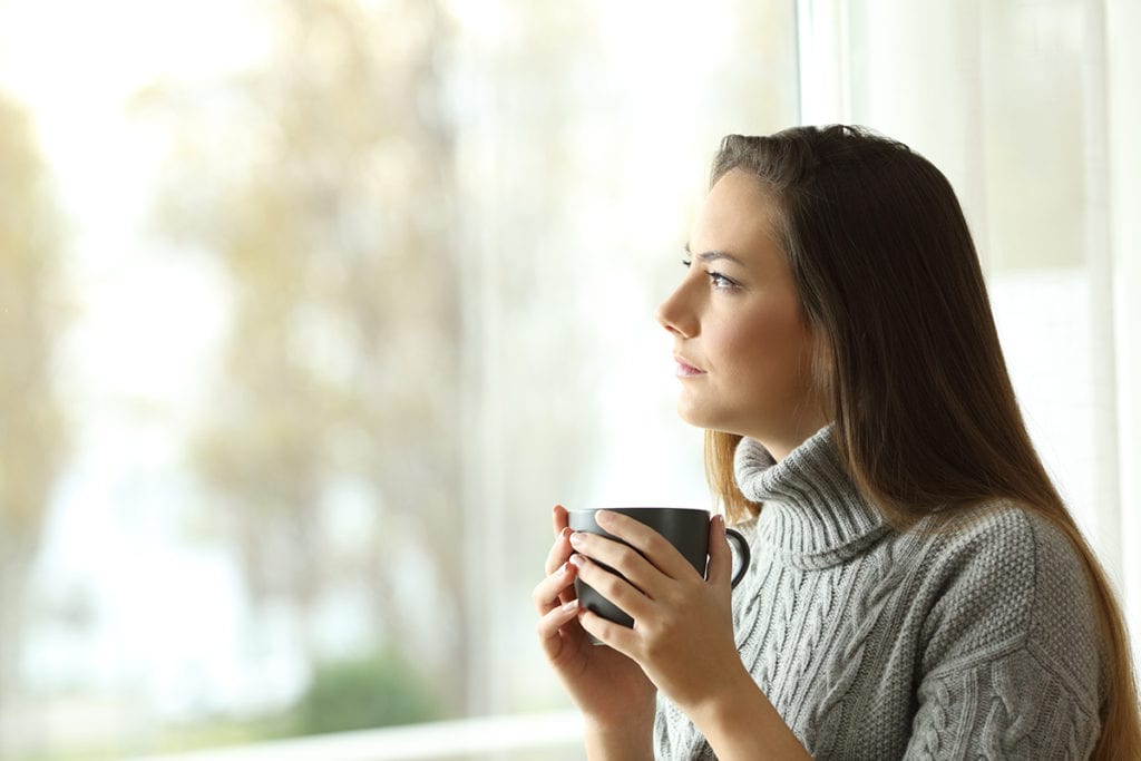 woman drinking tea and looking out the window avoiding Anxiety During a Pandemic
