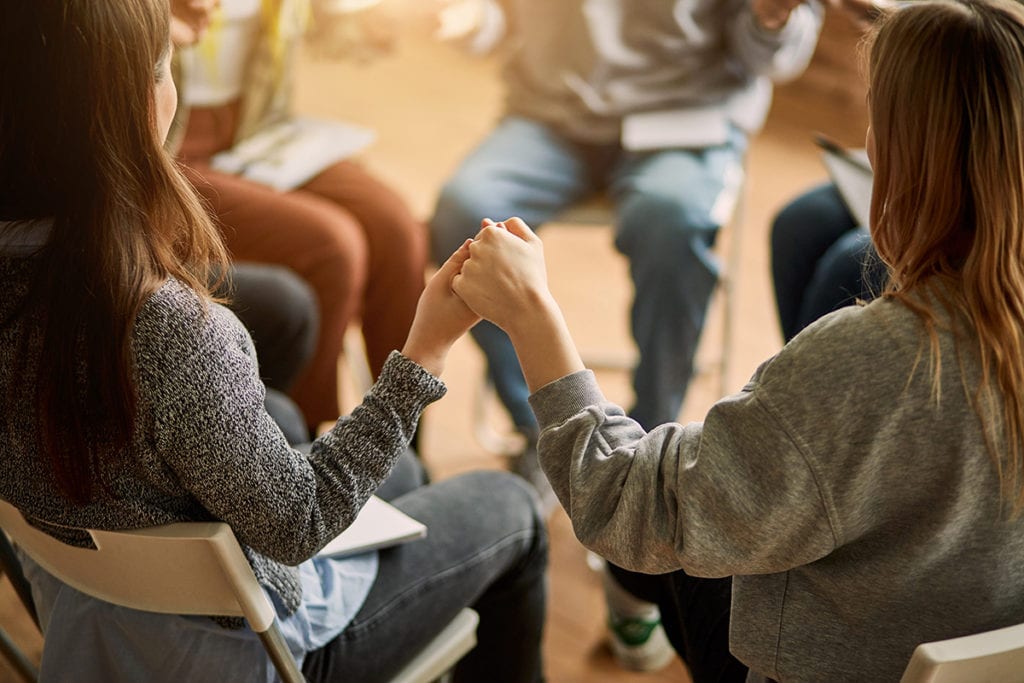women holding hands in a meeting about the Psychotherapy Definition in Addiction Counseling