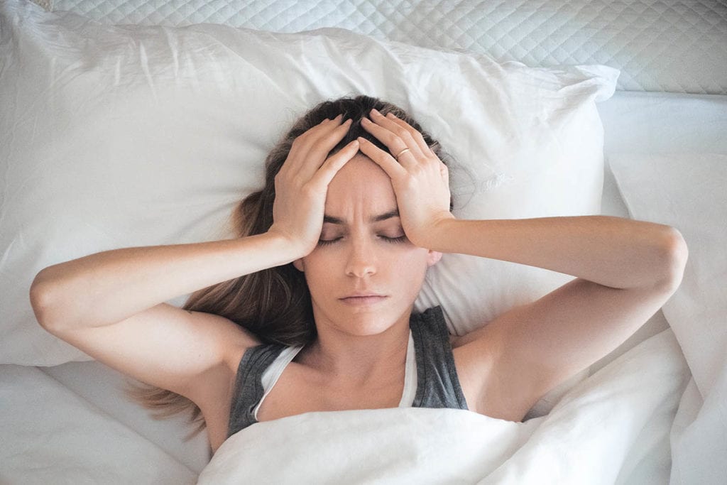 woman holding her head in bed feeling the Dangers of Mixing Substances