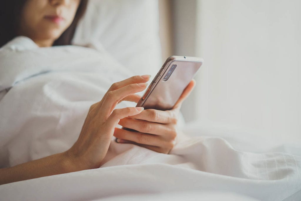 woman laying in bed on phone seeing the relationship of drinking and social media