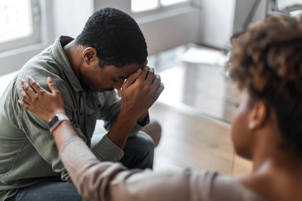 Man sits on couch and puts head in hands as she shows common signs of PTSD to family member