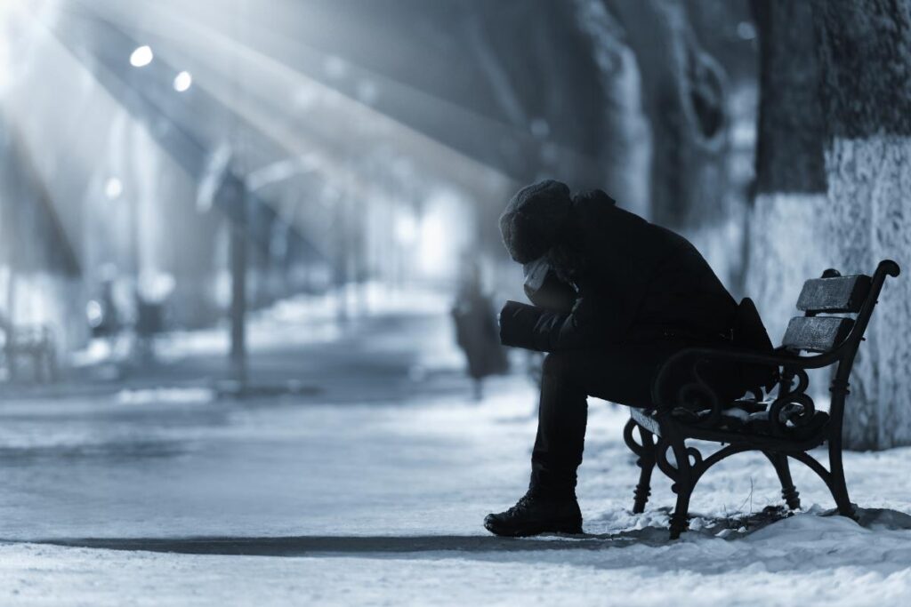 Woman sits on bench in winter as she wonders, "how does weather impact addiction?"